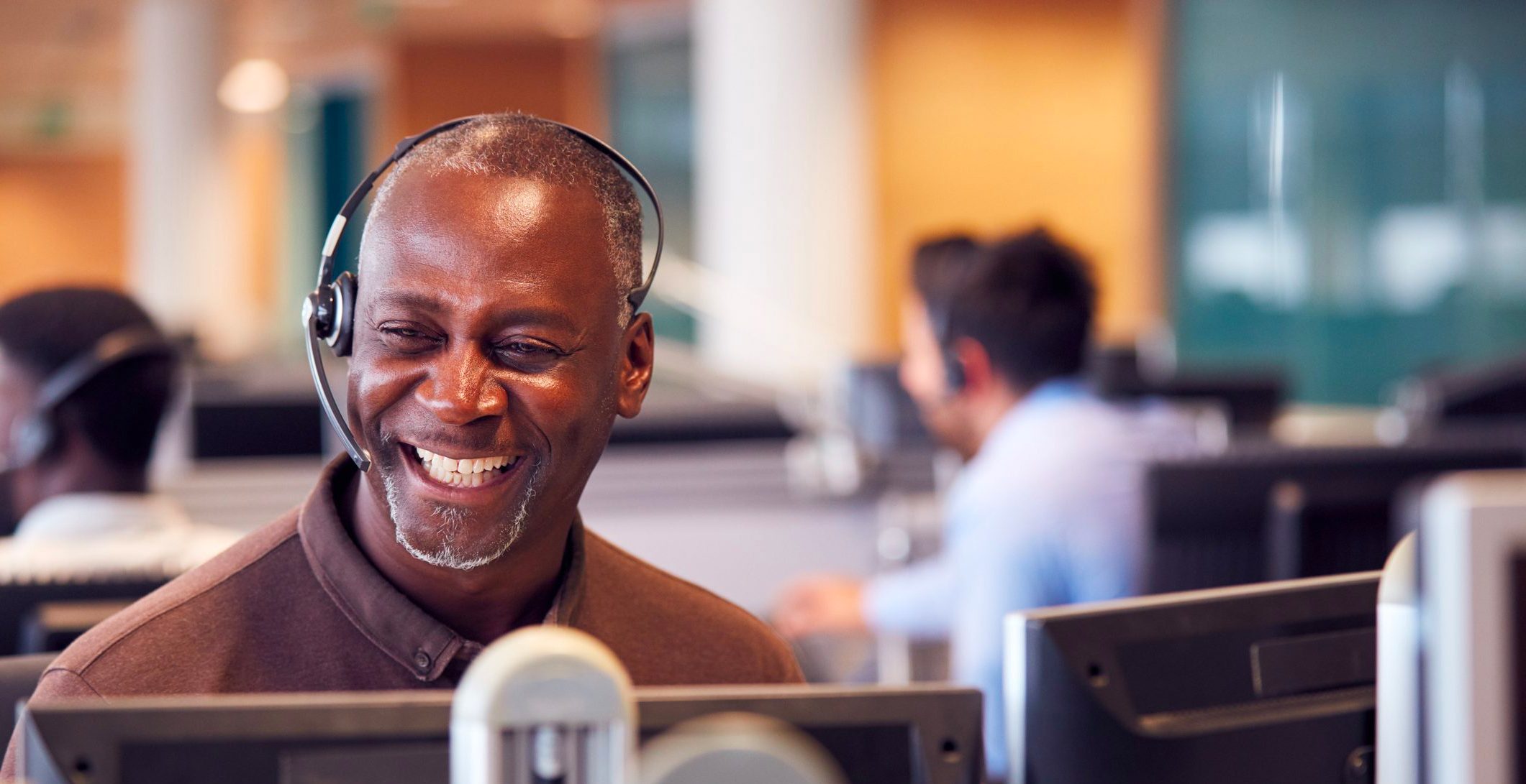 Mature Businessman Smiling Wearing Telephone Headset Talking To Caller In Customer Services Department
